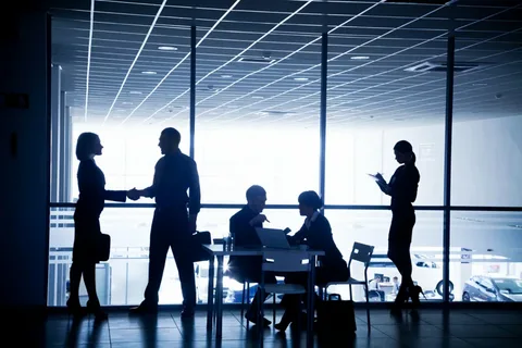 Silhouetted business professionals shaking hands in an office, representing corporate e-waste recycling and IT asset disposition partnerships.