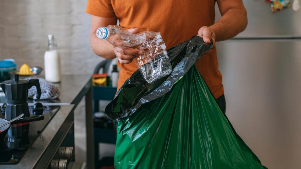Person separating plastic bottle into a recycling bag for eco-friendly waste management.