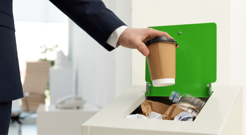 An office employee segregating a coffee cup into a recycling bin, showcasing corporate waste management solutions in Bangalore by Urbane Eco Recyclers.