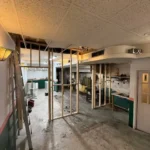 A step ladder positioned next to a partially dismantled false ceiling grid during a commercial salon strip-out.